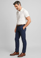 A man in a beige polo shirt and navy chinos stands, wearing brown dress shoes and a belt, with a subtle logo visible.