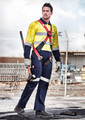 A man wears a yellow and navy rugged cooling overall with safety features. He holds a tool and stands in an industrial setting.