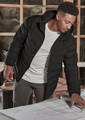 A black unisex puffer jacket with a hood, worn by a person examining blueprints indoors. The jacket has a logo.