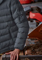 A grey unisex puffer jacket with a zip and pocket detail on the sleeve, displayed on a person near machinery.