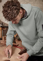 A unisex multi-pocket hoodie in green worn by a person working on wood, featuring a logo on the sleeve.
