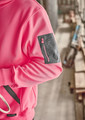A unisex water-resistant hoodie in pink with a grey zip pocket on the arm, set against a construction background.