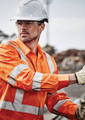 Hi-vis orange long sleeve work shirt with reflective tape, worn by a male worker in a construction setting, wearing safety gear.