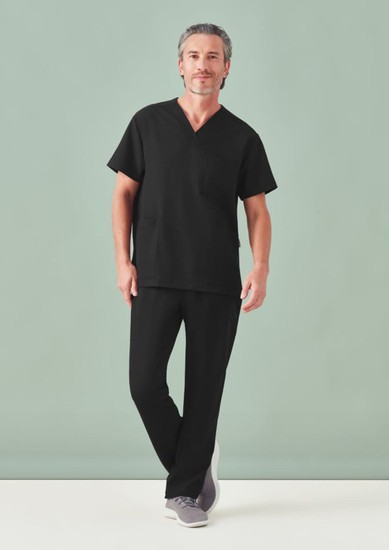 A man poses in black unisex scrub pants and matching short-sleeve top, with a plain background.