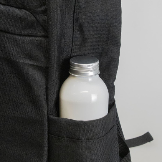 A black backpack pocket holds a silver-capped drink bottle, featuring a textured fabric design.