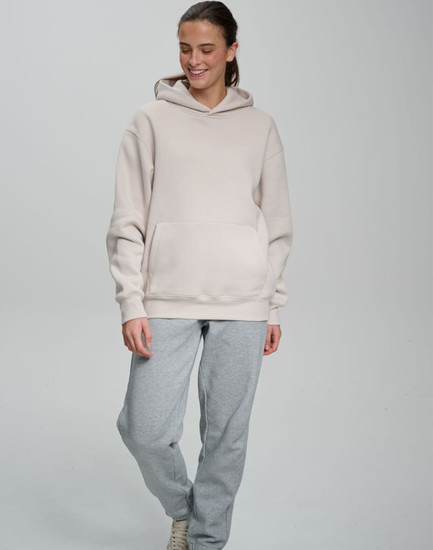 An oversized hoodie in a light beige colour, featuring a front pocket and a hood, paired with grey sweatpants.