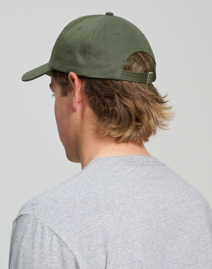 A green cotton twill unstructured cap viewed from the back on a person with long hair, wearing a grey shirt.