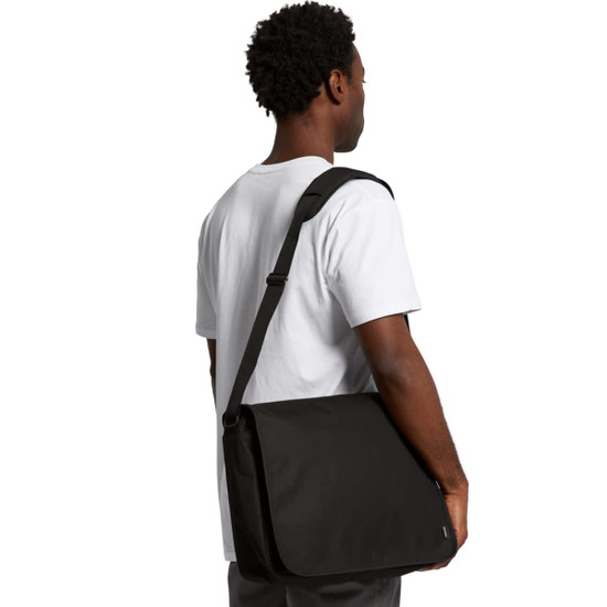 A man holds a black recycled messenger bag on his shoulder, featuring an adjustable strap and logo.