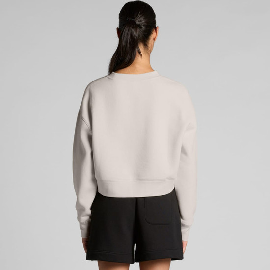 A light grey crop crew jumper viewed from the back, paired with black shorts. The design features a simple silhouette and a logo.