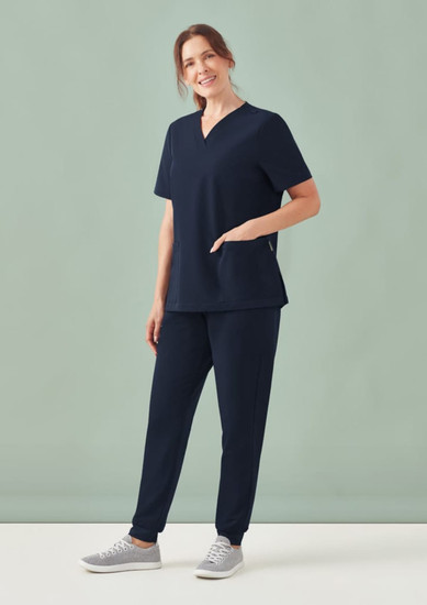 A woman stands wearing navy scrub pants and a matching top, featuring a pocket and a relaxed fit.