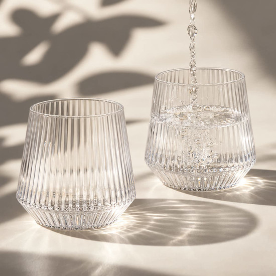 A drink bottle featuring a ribbed design, made of clear glass, with water being poured into two glasses.