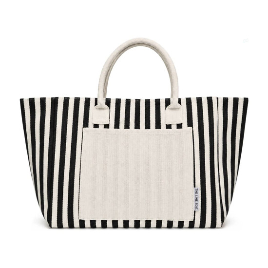 A striped tote bag in black and white with a plain cream-coloured front pocket and handles. It has a logo.
