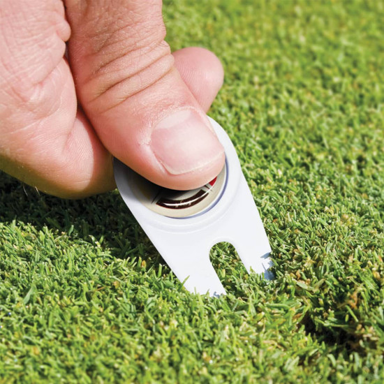 A golf divot repairer with a built-in marker, featuring a white casing, used for repairing grass on the green.