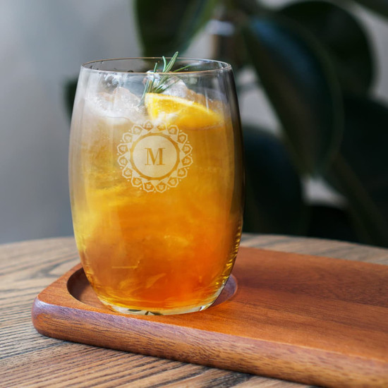 A HiBall glass filled with a golden drink, garnished with lemon and a sprig of rosemary, placed on a wooden tray.