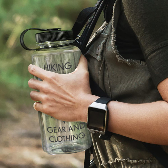 A drink bottle with a black lid and clear body, held against a person's torso in an outdoor setting.