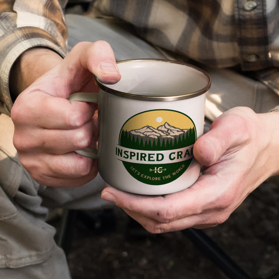 A mug in cream with a gold rim, featuring a nature-themed design and logo on the front.