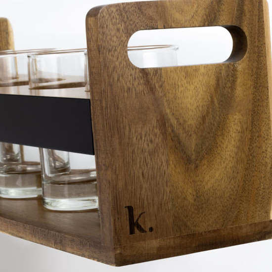 A wooden tray in a natural finish with a black band, holding several clear glass shot glasses, featuring a branding logo.
