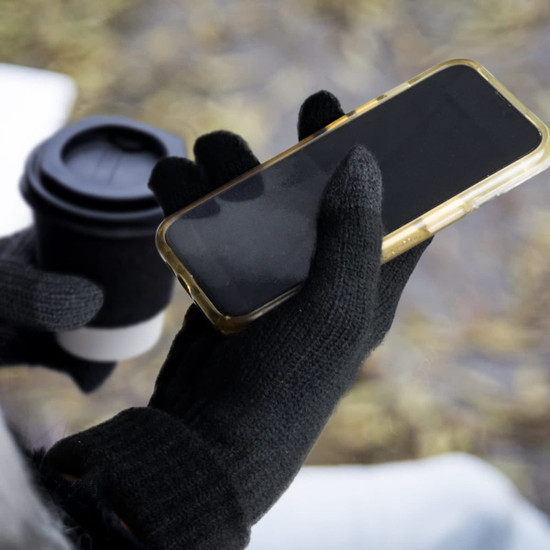 Black Himalayan Tech Gloves holding a smartphone, with a coffee cup partially visible in the background.