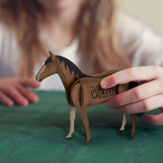 A wooden model of a horse in brown tones, featuring a logo, held by a person in the background.