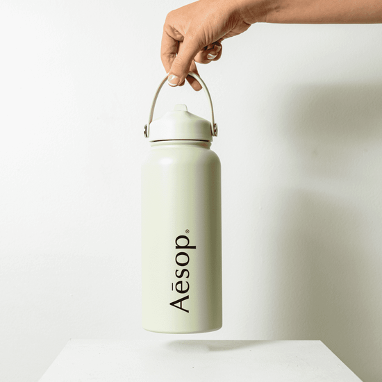 A drink bottle in a pale green colour, featuring a handle and a logo on the front.