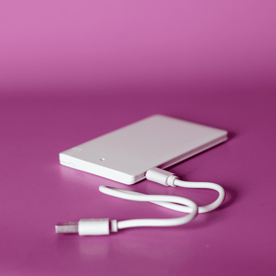 A white ultra slim power bank with a USB cable, set against a pink background.