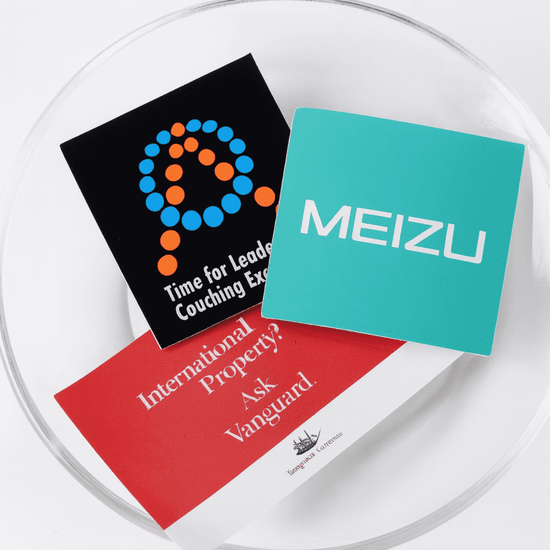 A bowl containing three vinyl stickers in various colours: black, teal, and white, featuring logos and text.