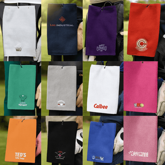 A collection of golf towels in various colours, each featuring different logos or branding.