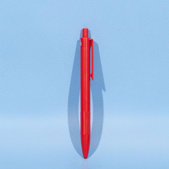 A red plastic ball pen stands upright against a light blue background, featuring a simple design and a logo.