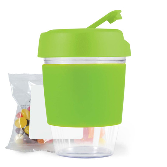 A reusable coffee cup with a bright green silicone sleeve and lid, accompanied by a small bag of colorful jelly beans.