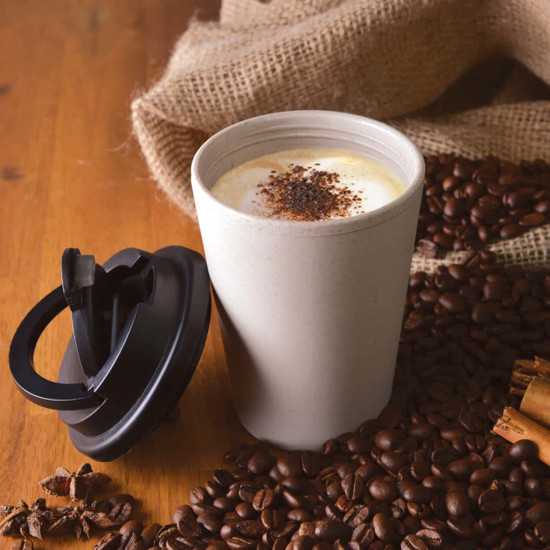 A reusable coffee cup in a light beige color with a black handle lid, surrounded by coffee beans and spices.