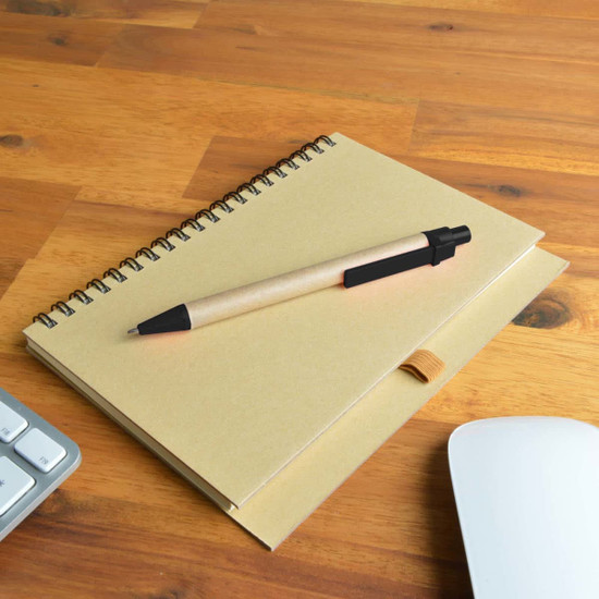 A tan notebook with a spiral binding and a black pen resting on top, placed on a wooden desk.