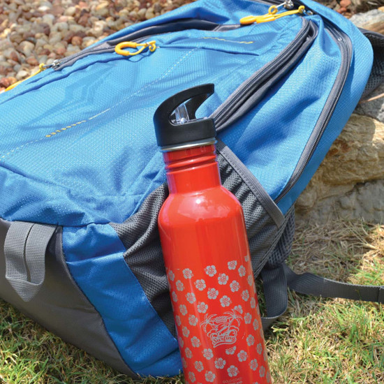 A red drink bottle with a black lid, featuring a floral pattern, next to a blue backpack.