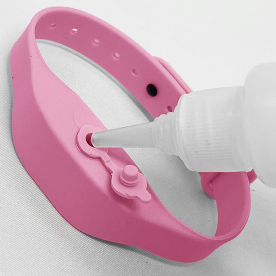 A pink wristband hand sanitiser dispenser with a nozzle dispensing sanitiser through a small opening.