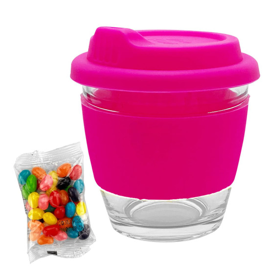 A reusable glass coffee cup with a bright pink silicone sleeve and lid, alongside a pack of colourful jelly beans.