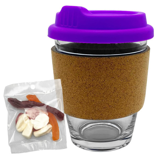 A transparent glass coffee cup with a purple lid and cork band, alongside a pack of mixed lollies.