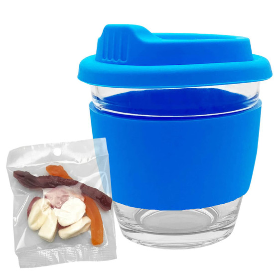 A glass coffee cup with a blue silicone lid and sleeve, paired with a packet of mixed jelly lollies.