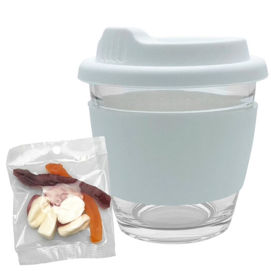 A glass coffee cup with a light blue silicone sleeve, accompanied by a pack of mixed jelly lollies in various colours.