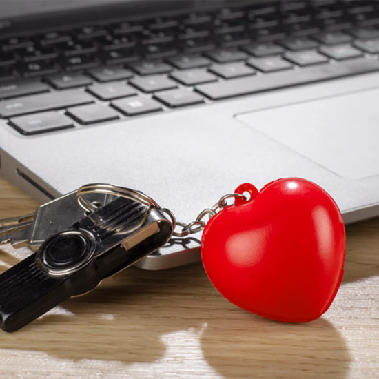 A red heart-shaped stress key ring attached to a set of keys, resting on a wooden surface near a laptop keyboard.