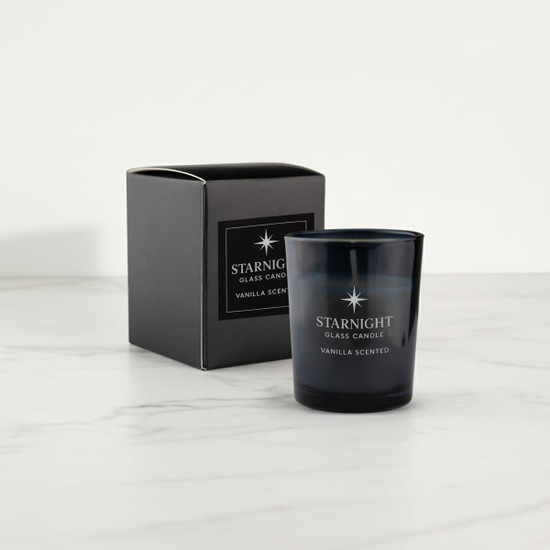 A black glass candle with a vanilla scent beside its black box packaging, set on a marble surface.