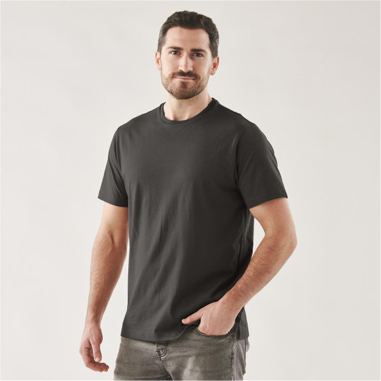 A man wearing a black short sleeve t-shirt, standing confidently with one hand in his pocket. The shirt has a logo.