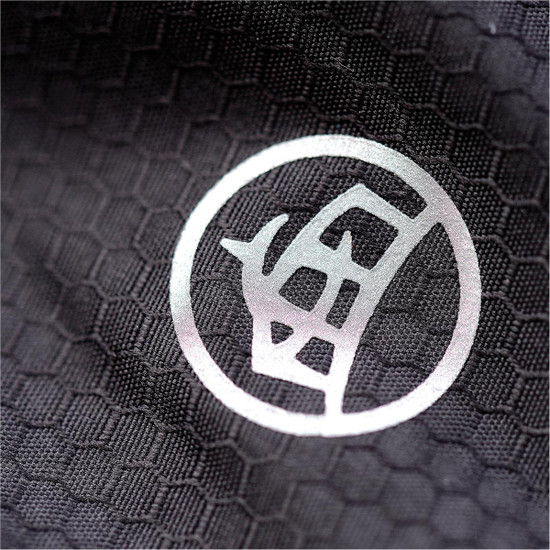 A close-up of a black textured fabric featuring a circular logo. The texture resembles a honeycomb pattern.
