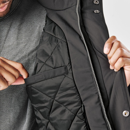 A man shows the interior pocket of a black thermal jacket, featuring a quilted lining and a hood.