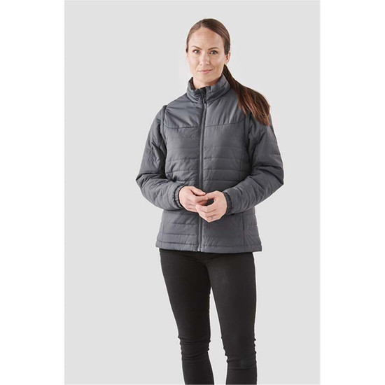 A woman wearing a grey insulated jacket with a zip front and stands against a light background.