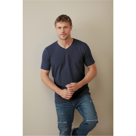 A man wearing a navy blue V-neck t-shirt, paired with ripped jeans, standing against a neutral background.