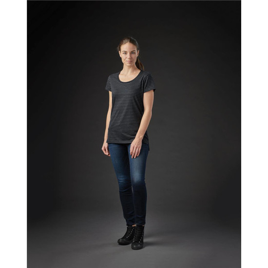 A woman stands in a fitted black and grey striped crew neck t-shirt, paired with dark jeans and ankle boots.
