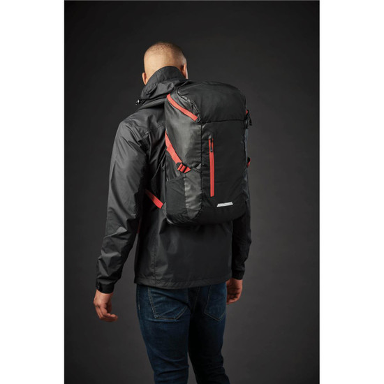 A black and red backpack is worn on the back of a person in a jacket, with various pockets visible.