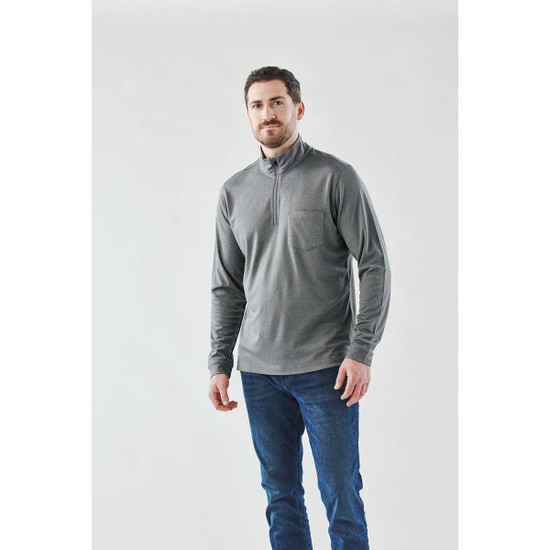 A man wearing a grey 1/4 zip pullover, paired with blue jeans, against a light background. The pullover has a pocket and branding.