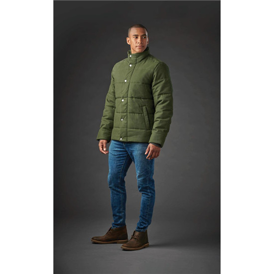 A man stands wearing a green thermal jacket with a buttoned front, paired with jeans and boots. The background is grey.