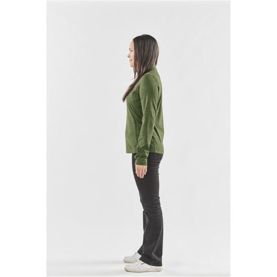A woman stands in profile, wearing a green performance jacket and black trousers, with a logo visible on the jacket.