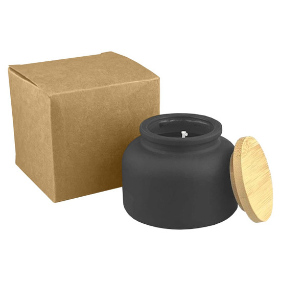 A black candle in a round jar with a bamboo lid, accompanied by a brown cardboard box.